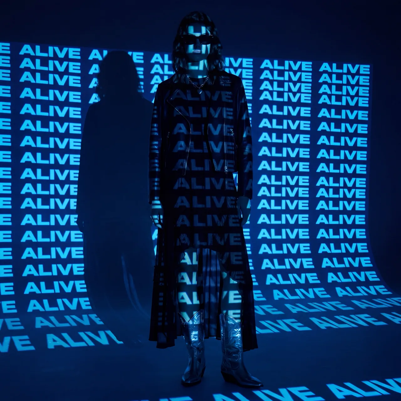 Model in a long black coat under an ALIVE projection in blue light