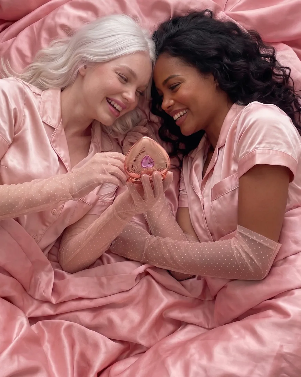 Charlotte Tilbury beauty concept campaign, two models in pink silk sharing a blush compact