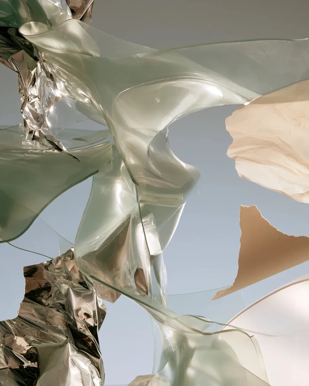 Abstract material study: sage-green translucent film, silver mylar and torn oat paper draped into sculptural folds against a pale sky