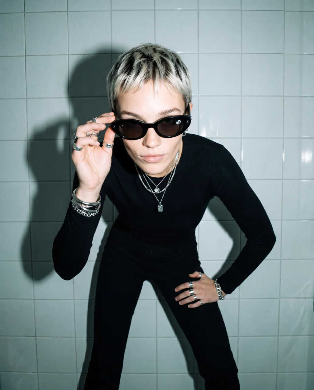 Meta smart glasses concept campaign, model leaning forward in black against tiled walls