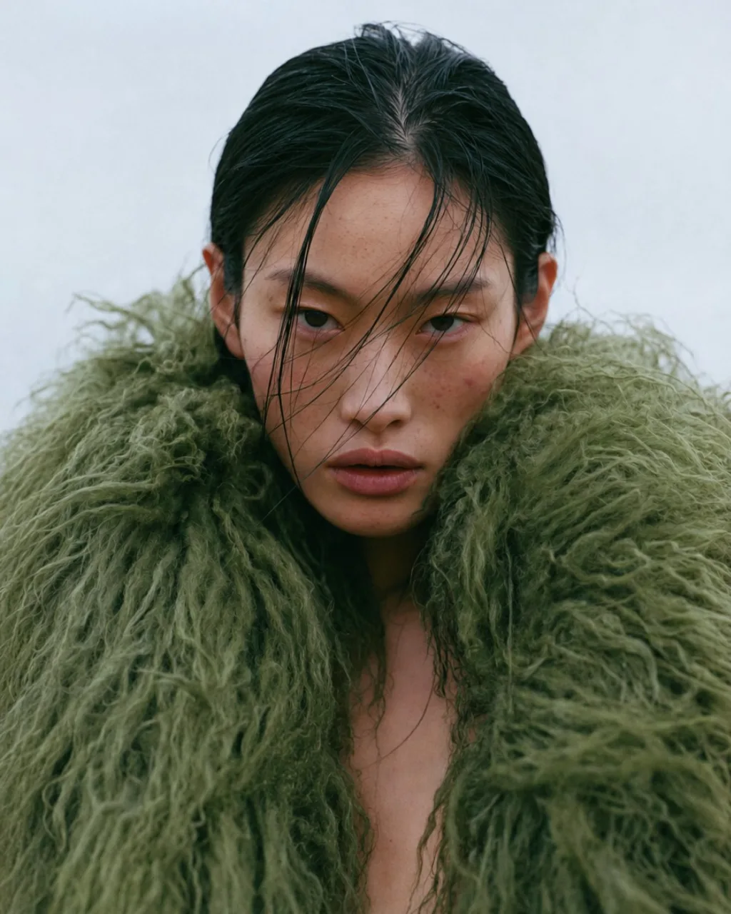 Model in a green shearling coat against a grey sky