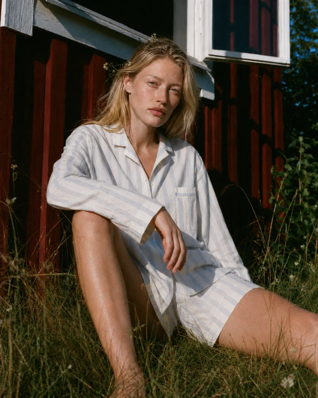 Woman in a striped linen shirt sitting in the grass by the cabin