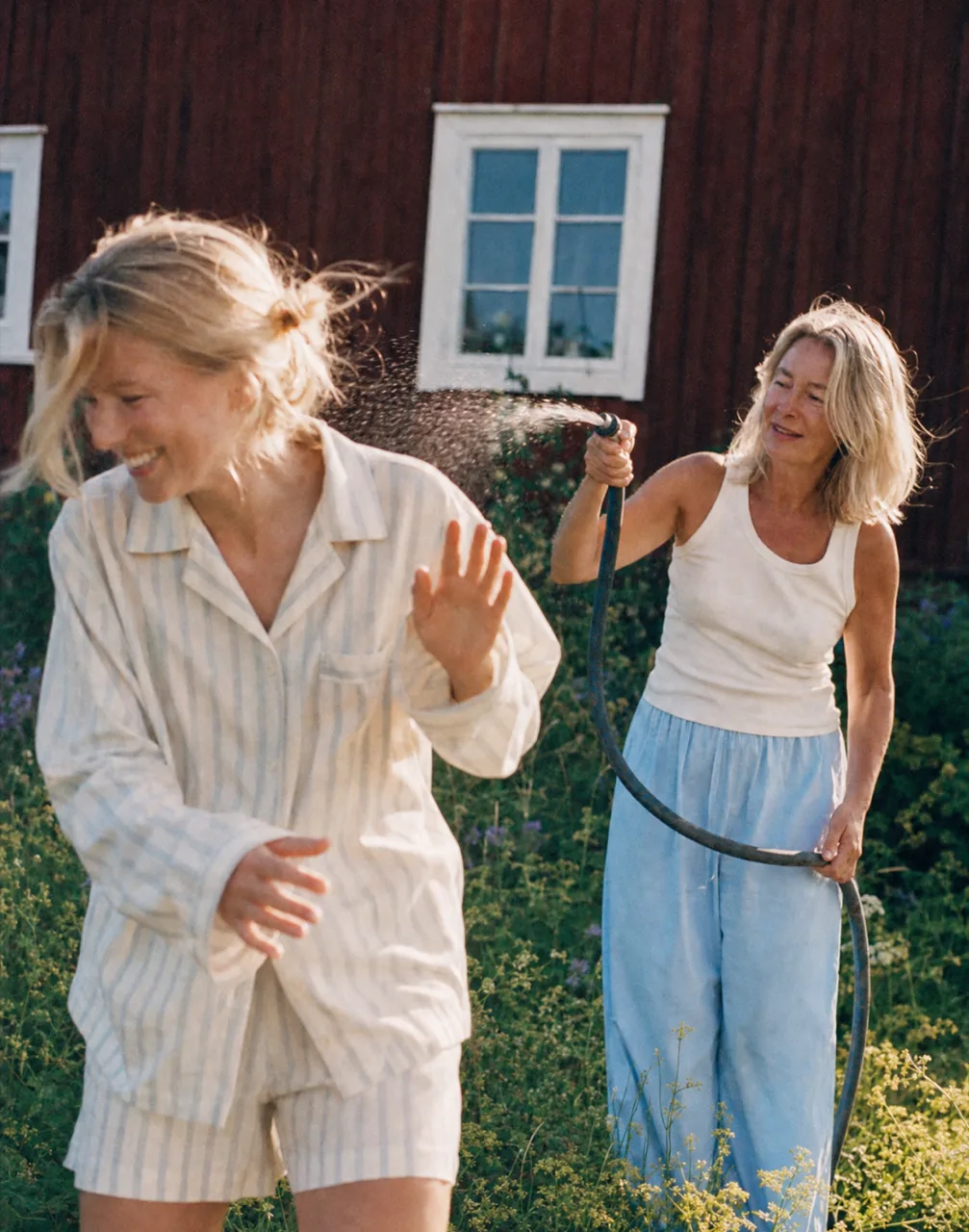 Two women laughing as one sprays a garden hose outside the cabin
